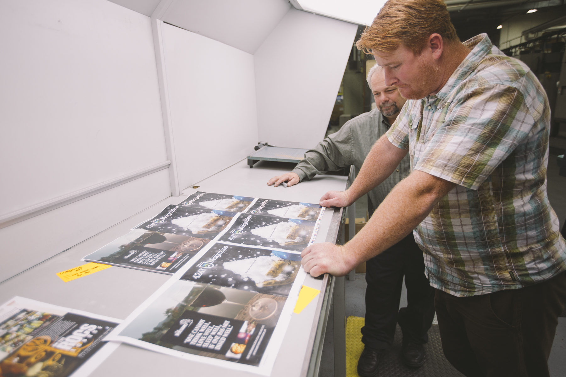 Two press operators checking a printed press sheet of 4241 Magazine on a light table during the print run