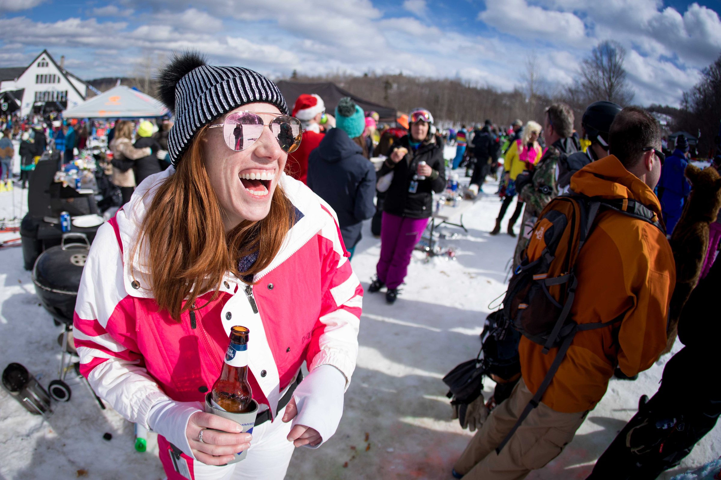 A guest laughing at a sunny base-area gathering, crowd behind — the place, alive and social all season