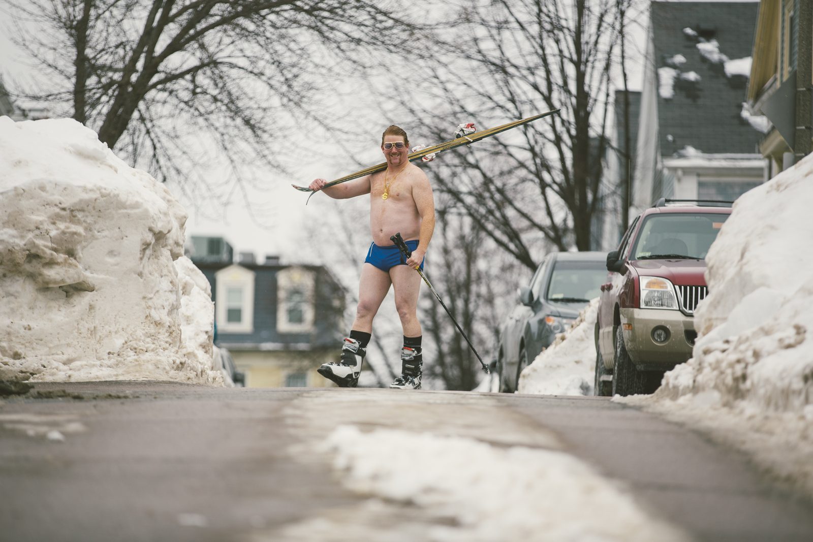 The King strutting a snowbanked street with old skis over his shoulder — like he owned the place